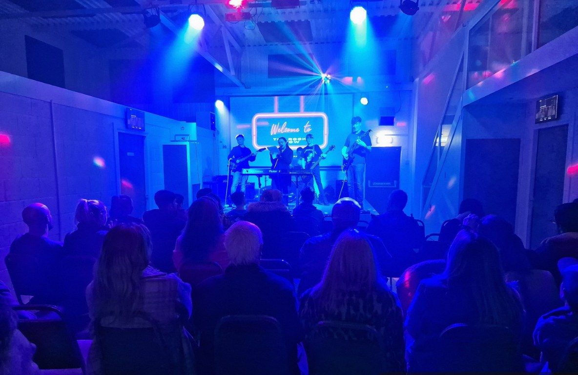A band playing on the hall stage to a crowd on a Friday gig night